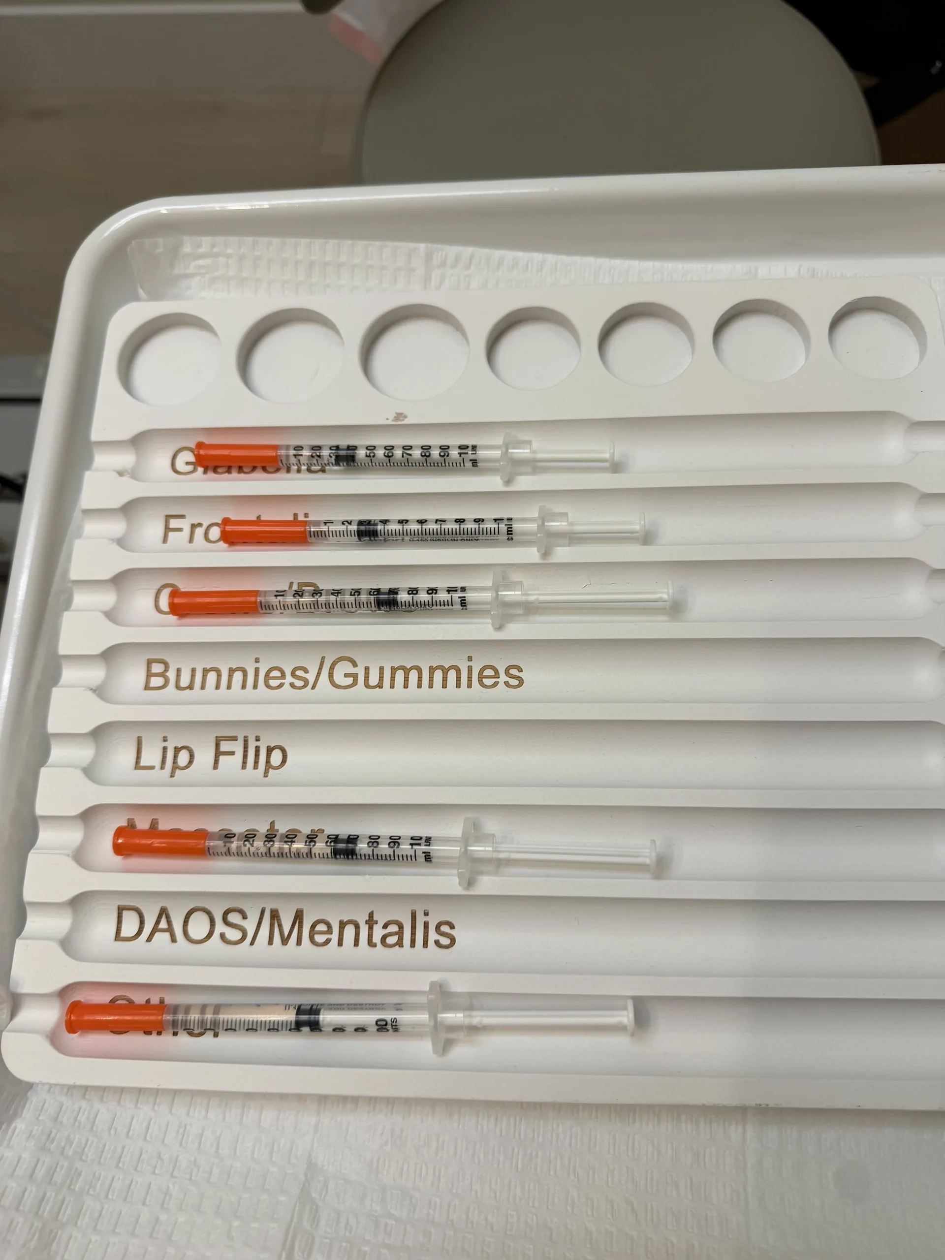 Prepared syringes on a tray labelled by treatment area, including bunny lines, lip flip and DAO and mentalis