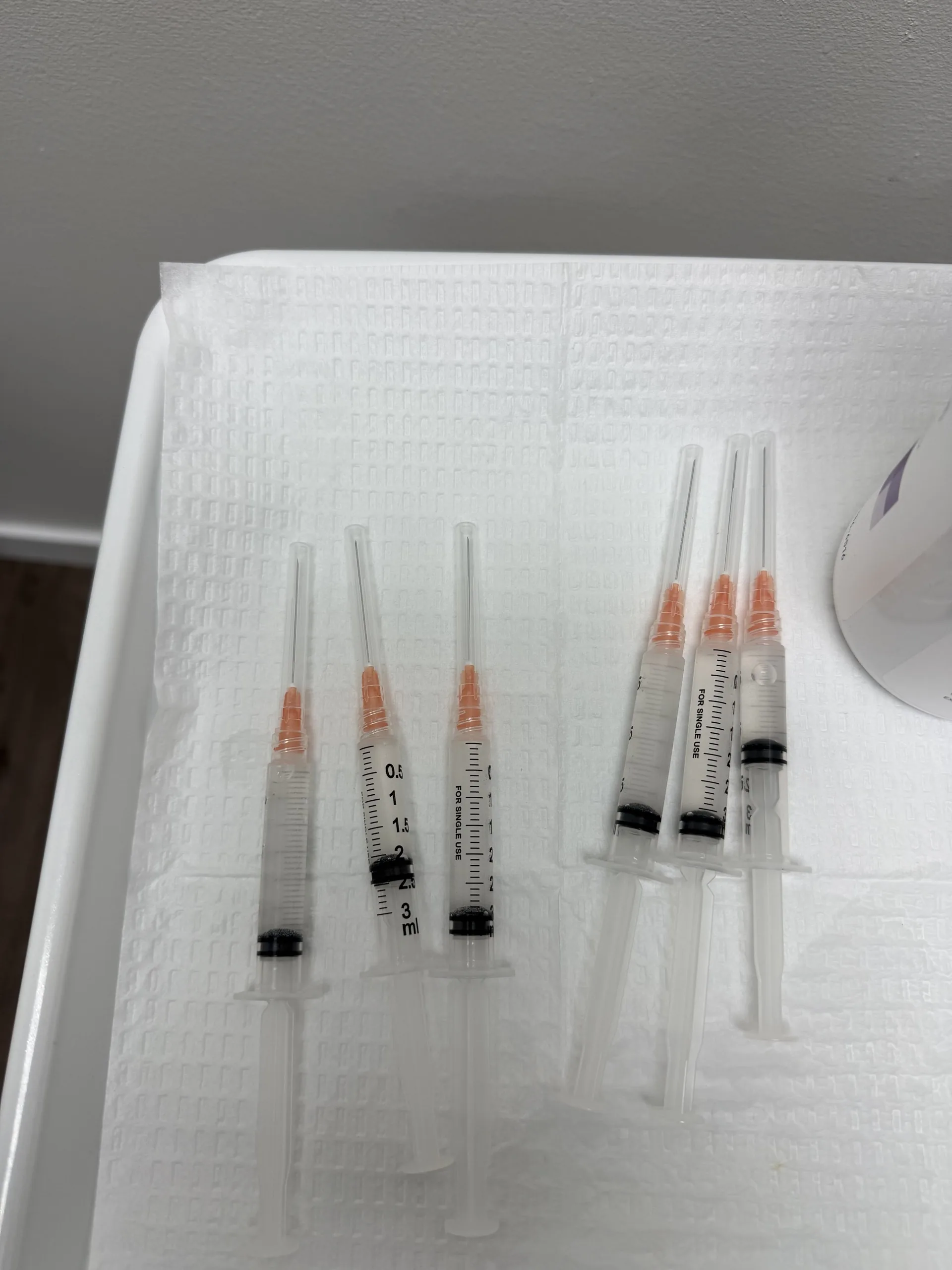 Six syringes with orange needle caps laid out on a treatment tray