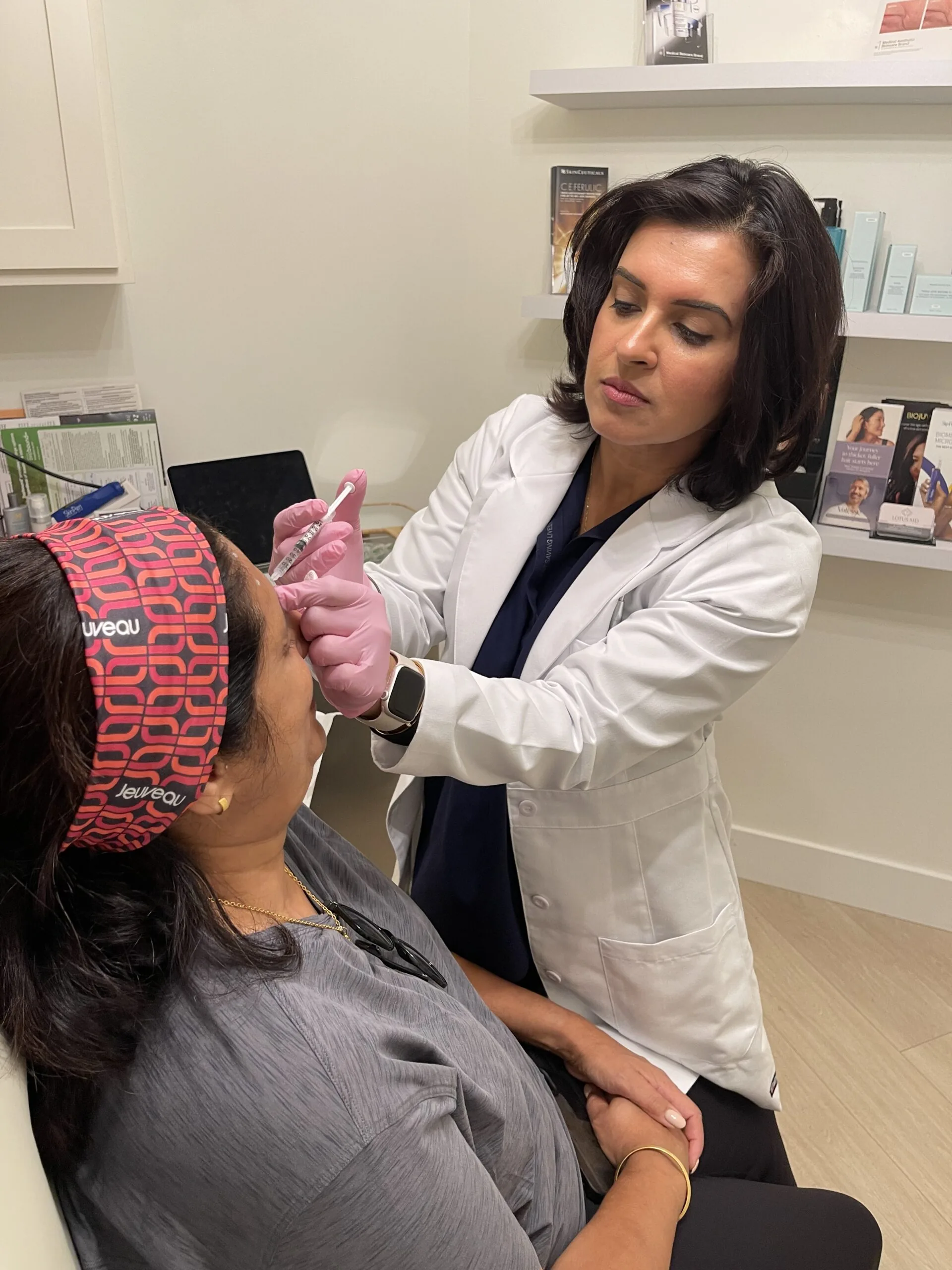 A physician in a white coat giving an injection to a seated patient's forehead