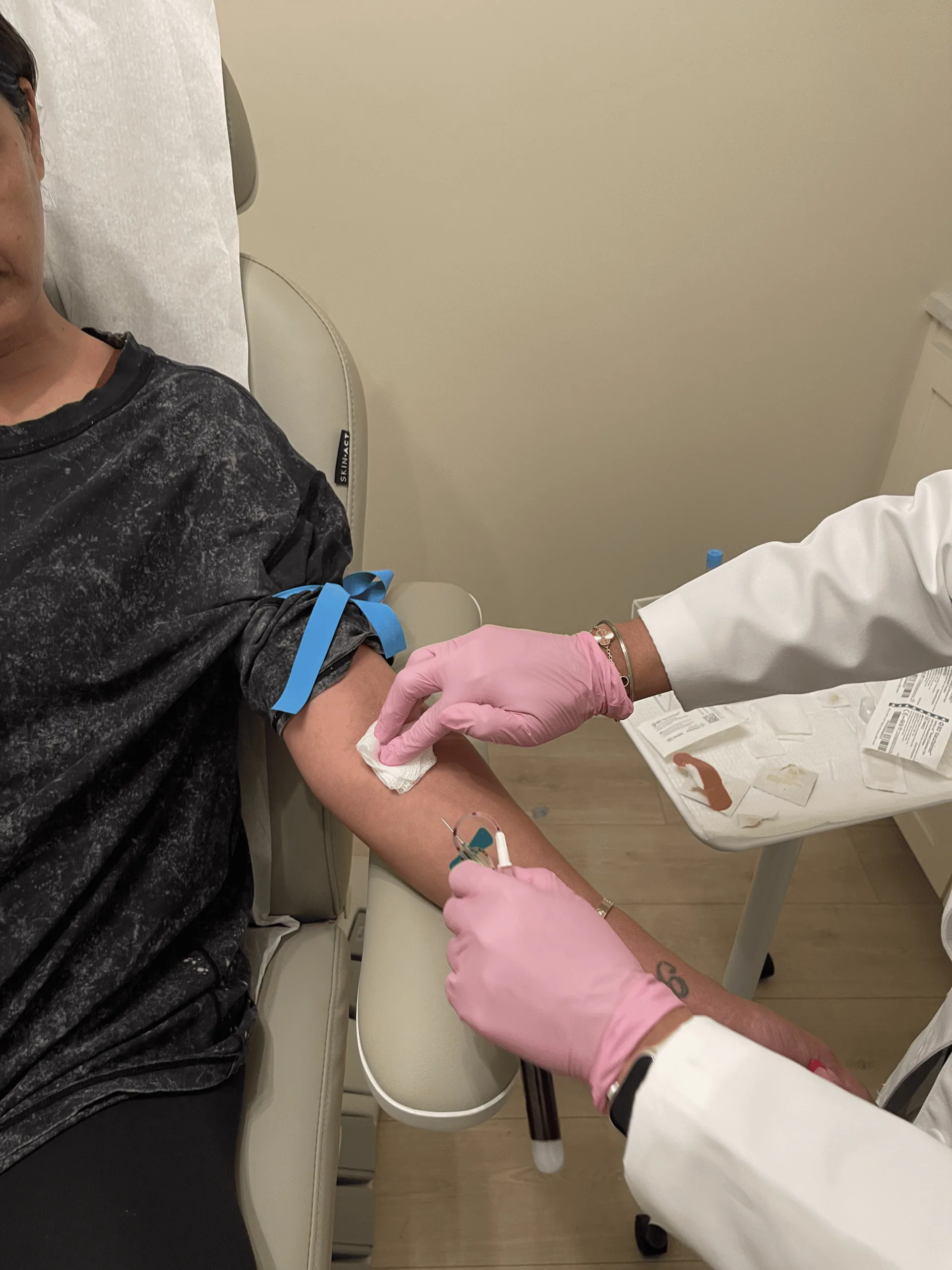 A clinician in pink gloves drawing blood from a patient's arm in the clinic