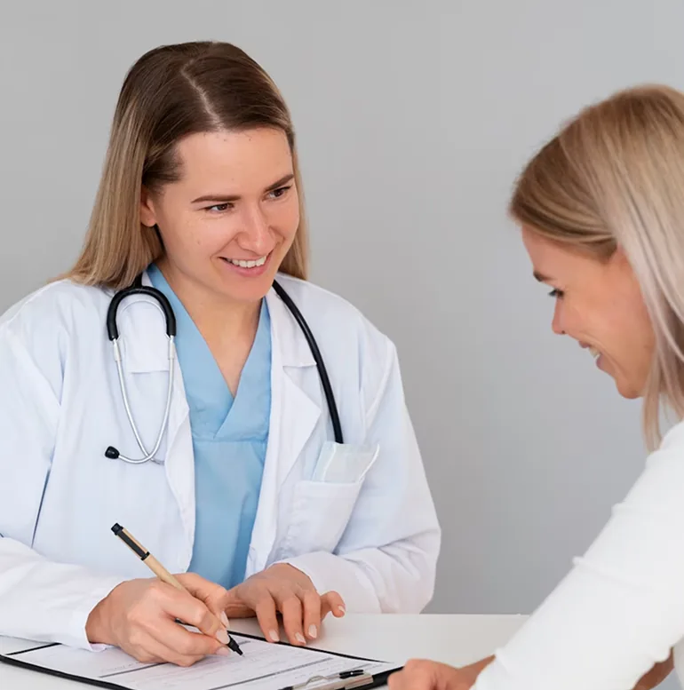 A physician in a white coat taking notes while talking with a patient