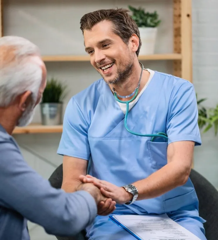 A clinician in blue scrubs holding an older patient's hand during a visit