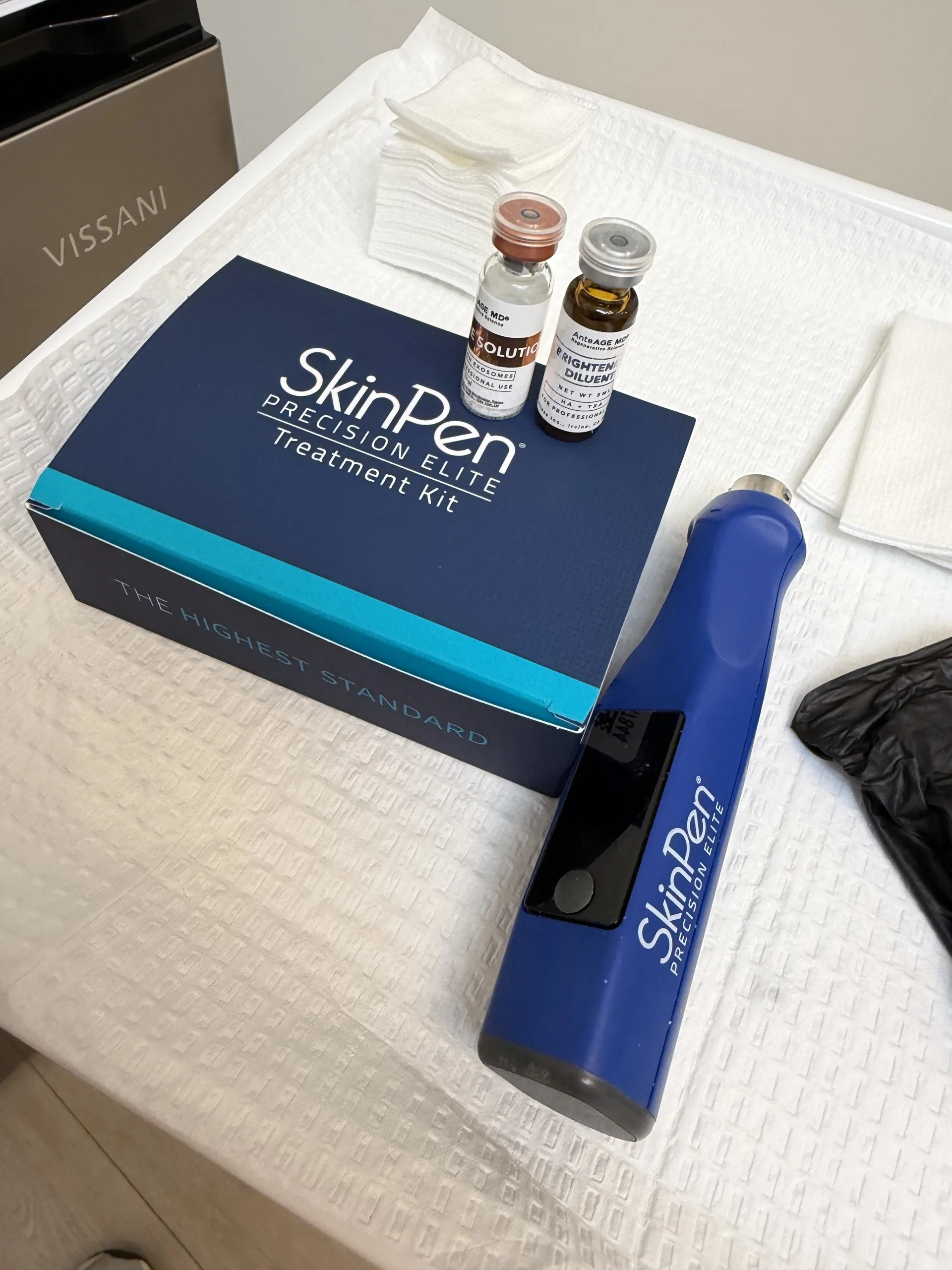 A SkinPen Precision Elite pen and treatment kit with two vials, including an exosome vial, on a treatment table