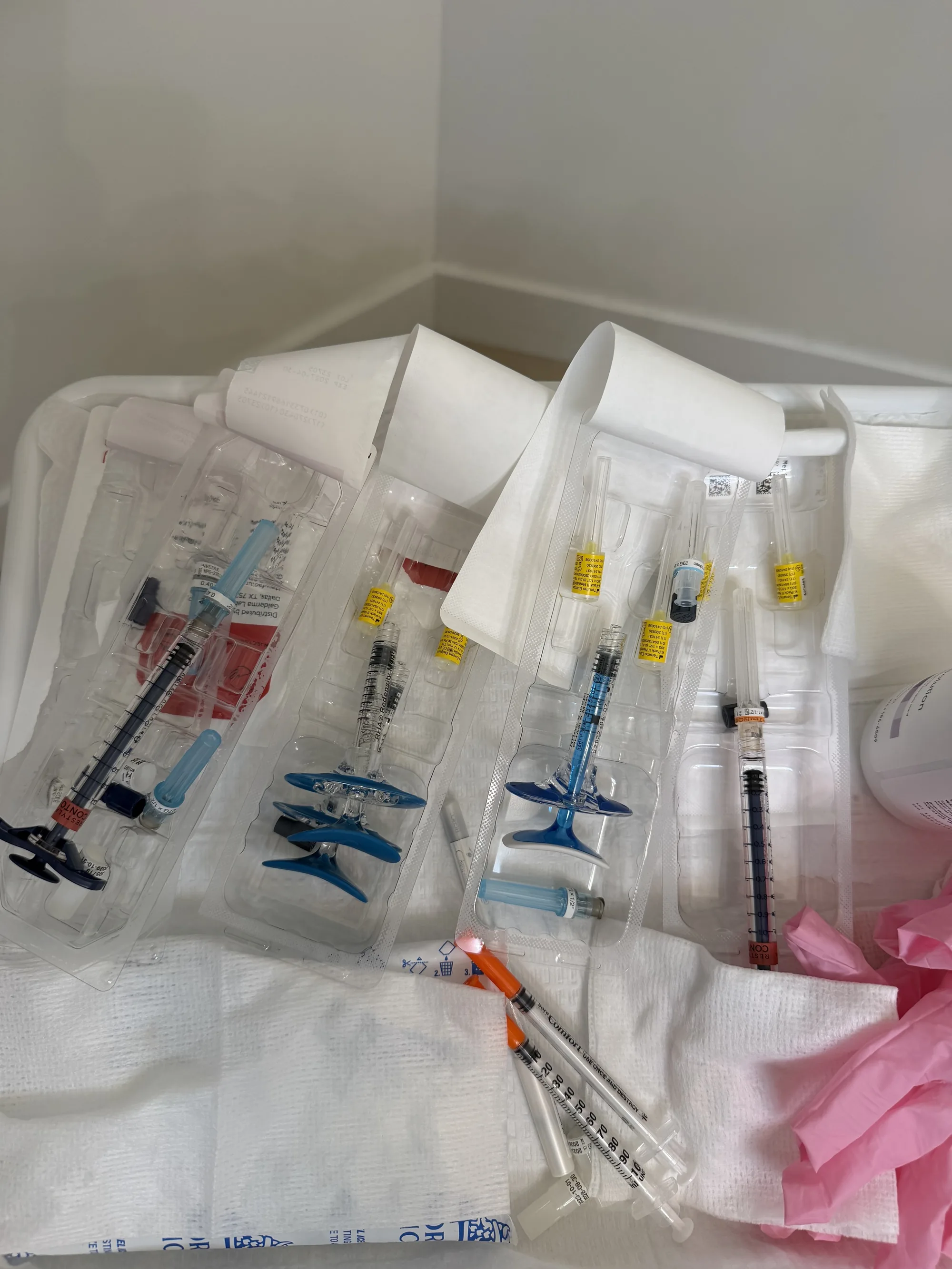 Several prefilled injectable syringes in their opened plastic trays on a treatment tray, with pink gloves to the side