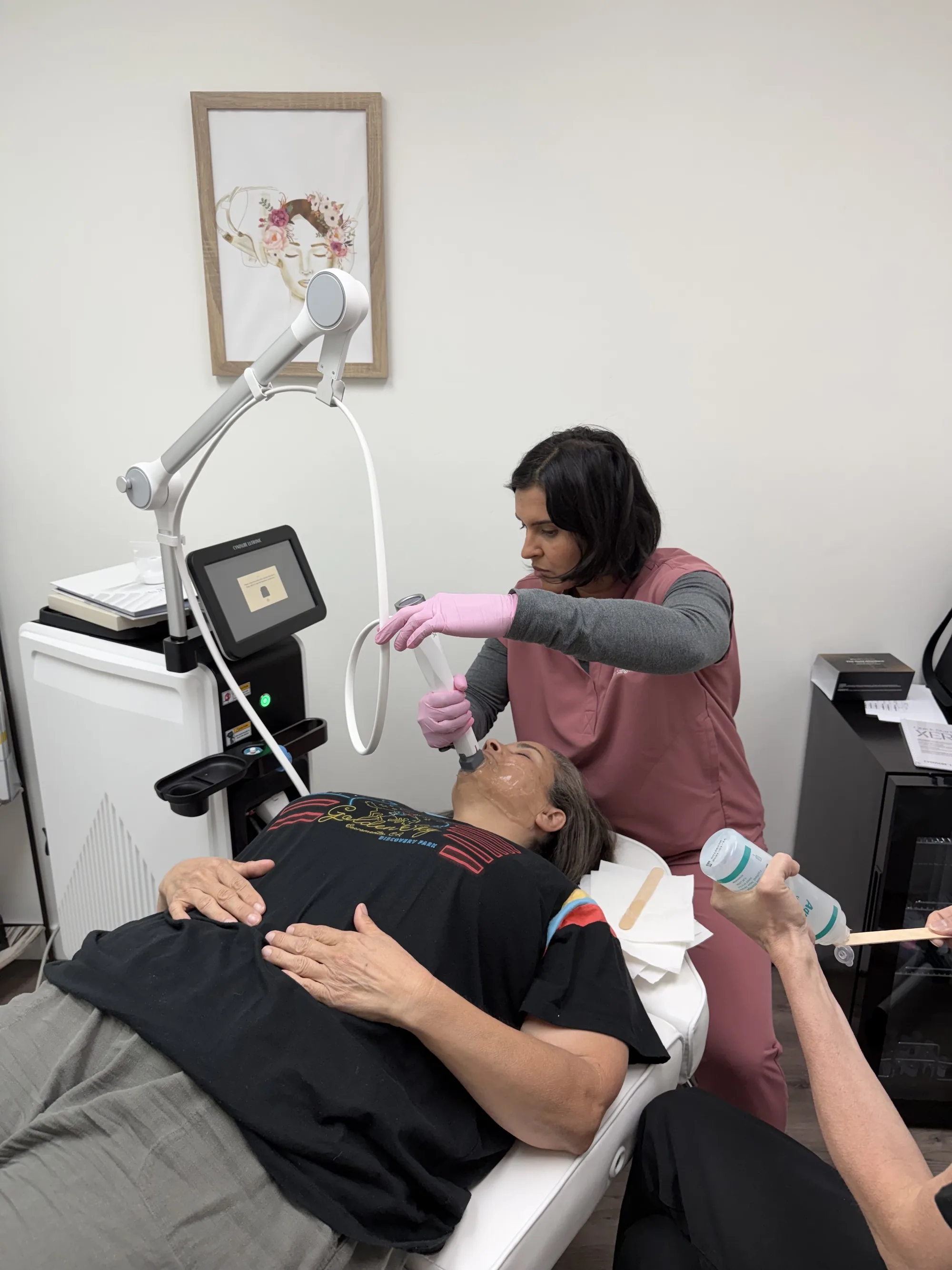 A provider in pink scrubs treating a reclining patient’s face with the XERF handpiece